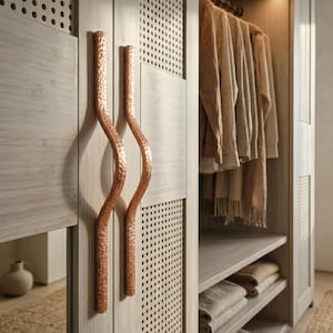 May include: A light wood-toned closet with copper-colored, wavy handles. The closet doors have a perforated design. Inside, clothes hang on a rod, and folded items sit on shelves. A woven rug is on the floor.