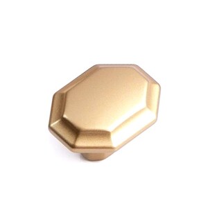 Könnte beinhalten: Ein goldfarbener, facettierter Schrankknauf mit geometrischem Design. Der Knauf hat eine flache, achteckige Fläche und einen abgerundeten Sockel. Die Oberfläche ist matt und verleiht ihm einen dezenten Glanz. Geeignet für Schubladen und Schränke.