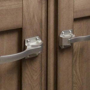 Peut inclure: Gros plan de deux poignées de placard en nickel brossé montées sur une porte de placard en bois. Les poignées ont un design incurvé et sont fixées avec des plaques de montage carrées. Le grain du bois est visible.