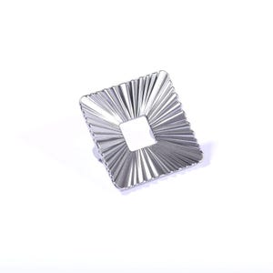Op de afbeelding: Een zilverkleurige, vierkante kastknop met een centrale vierkante uitsparing. De knop heeft een gestructureerd, stralend ontwerp, waardoor een zonnestraaleffect ontstaat. De hardware is ontworpen voor meubels en woondecoratie.
