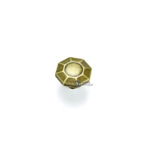 Puede incluir: Un tirador de armario de color latón antiguo con forma octogonal y centro circular. El tirador tiene una estética vintage y probablemente está hecho de metal. El herraje está diseñado para muebles.