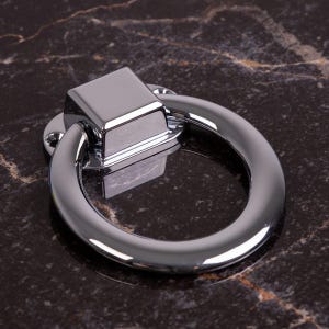 Könnte beinhalten: Ein polierter Chrom-Schrankgriff mit quadratischer Basis und rundem Griff. Die Hardware ist reflektierend, mit dunklem Hintergrund. Der Griff ist für einfaches Greifen und Öffnen von Schubladen oder Schränken konzipiert.