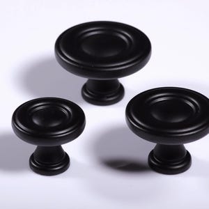 Op de afbeelding: Een witte keramische mok met een zwart handvat en de tekst "But First, Coffee" in een handschriftstijl. De mok staat op een wit oppervlak. De mok is ongeveer 10 cm hoog.