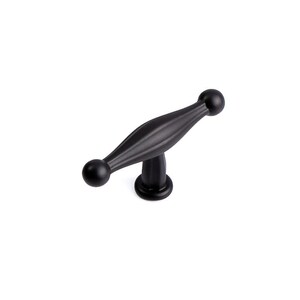 Puede incluir: Un tirador de armario negro con un diseño decorativo. El tirador presenta un cuerpo central alargado con extremos redondeados y una base circular. El herraje es de metal y está diseñado para su uso en cajones o armarios.