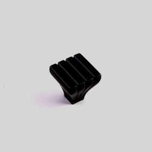 Pode incluir: Um puxador de armário preto com um design único. O puxador apresenta quatro barras retangulares verticais na parte superior, com uma base alargada. A ferragem é feita de um material escuro e sólido, sobre um fundo cinza claro.