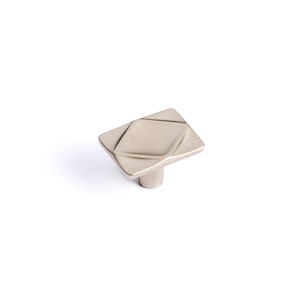 May include: A brushed nickel square cabinet knob with a geometric design. The knob has a diamond pattern on its face and a cylindrical base. The hardware is set against a white background.