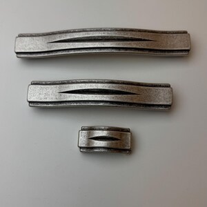 May include: Three antique-style cabinet pulls in varying sizes. The pulls have a textured, silver finish with a subtle wave design. The largest pull is approximately 10 inches long, the medium is 6 inches, and the smallest is 2 inches.