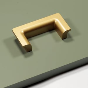 Peut inclure: Une poignée de meuble dorée de forme rectangulaire. La poignée est posée sur une surface vert sauge, projetant une ombre. La quincaillerie a une esthétique moderne et minimaliste, adaptée aux meubles ou aux armoires.