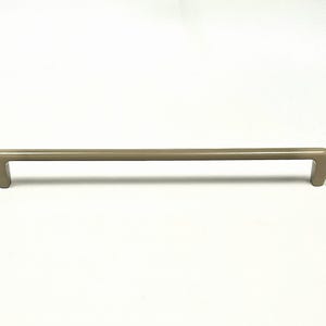 Op de afbeelding: Een taupekleurige kastgreep met een rechte stang en gebogen uiteinden. De hardware is gemaakt van metaal en is ontworpen voor laden of kastdeuren. De greep is ongeveer 30 cm lang.