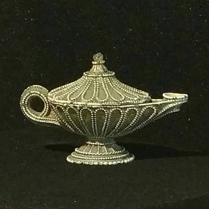 May include: A decorative genie lamp with a white and gold finish. The lamp has a round base and a spout with a handle. The lamp is made of ceramic and has a detailed design.