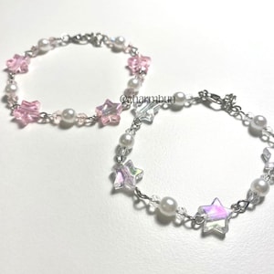 May include: Two delicate bracelets. One features pink star-shaped beads and white pearls, the other has iridescent star beads and white pearls. Both are strung on a silver chain. The text "@charmbun" is visible.