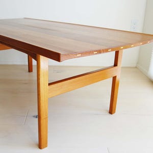 May include: A rectangular wooden coffee table with a light brown finish. The table has four legs and a simple, minimalist design. The table is approximately 48 inches long, 24 inches wide, and 16 inches high.