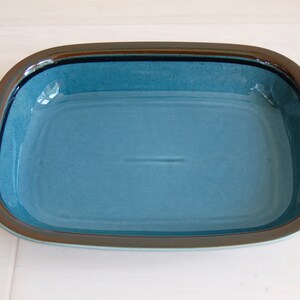 May include: A blue ceramic baking dish with a brown rim. The dish is empty and has a slight sheen.