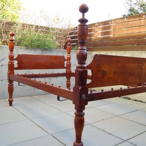 May include: A wooden bed frame with four posts, a headboard, and a footboard. The bed frame is made of dark wood and has a simple design.