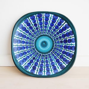Peut inclure: Une grande assiette en céramique ronde de couleur bleu et verte avec un motif géométrique. L'assiette a un centre surélevé avec un cercle plus petit au milieu.