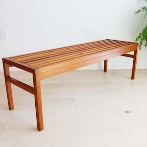 May include: A wooden bench with a slatted top and a natural wood finish. The bench has a simple, modern design and is perfect for adding a touch of rustic charm to any space.