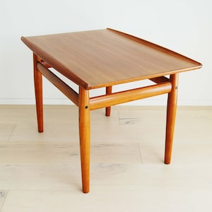 May include: A mid-century modern side table with a rectangular top and four tapered legs. The table is made of wood with a warm, natural finish. The table measures approximately 24 inches long, 16 inches wide, and 20 inches high.