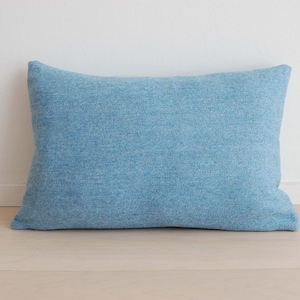 May include: A rectangular throw pillow in a solid light blue color. The fabric features a visible woven texture with subtle variations in the blue thread, creating a soft, heathered appearance across the entire surface of the pillow cover.