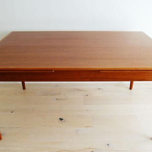 May include: A rectangular wooden dining table with a smooth, medium-brown finish. The table features a flat top with a visible wood grain pattern and four tapered, cylindrical legs that extend outward from the corners to provide support.