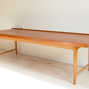 May include: A mid-century modern wooden coffee table. The rectangular table has a light brown oak base and a darker brown tabletop. The table is approximately 60 inches long, 18 inches wide, and 16 inches high.