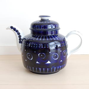 May include: A ceramic teapot featuring a deep blue glaze with white hand-painted circular and vertical line patterns. The teapot has a white handle, a white spout decorated with blue dots, and a matching lid with a small knob on top.
