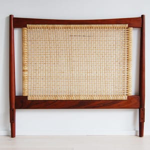 May include: A mid-century modern headboard with a woven cane center and a dark wood frame. The headboard has a rectangular woven cane panel and a solid wood frame. The headboard is designed to be placed against a wall.