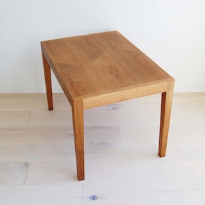 May include: A rectangular wooden table with a natural finish. The table has four straight legs and a simple design. The wood grain is visible on the tabletop and legs. The table is approximately 30 inches long.
