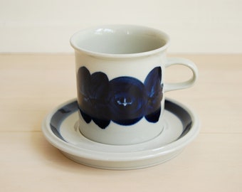 May include: A white ceramic coffee cup with a blue floral design. The cup is sitting on a matching saucer.