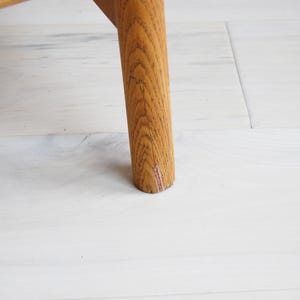 May include: Close-up of a wooden furniture leg. The leg is cylindrical, made of light brown wood with visible grain. The leg is set against a white wooden floor.