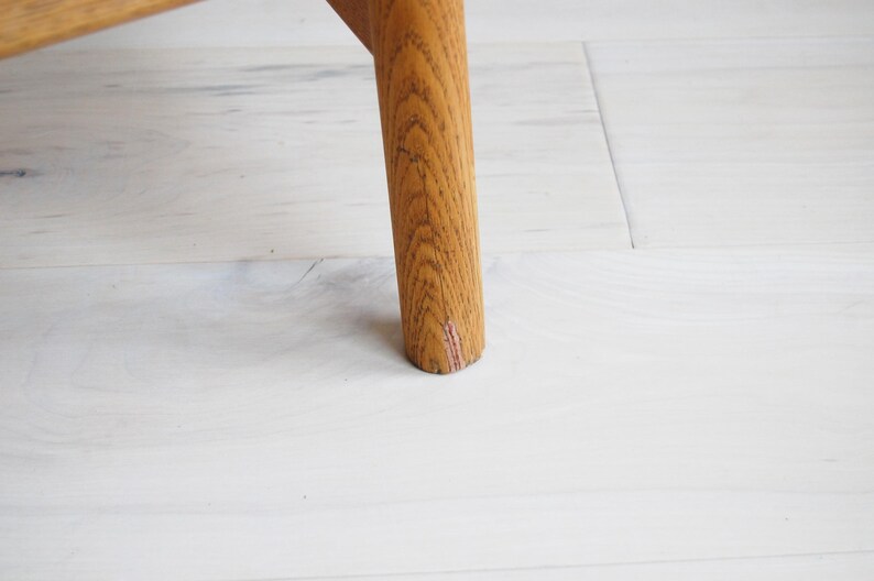 May include: Close-up of a wooden furniture leg. The leg is cylindrical, made of light brown wood with visible grain. The leg is set against a white wooden floor.