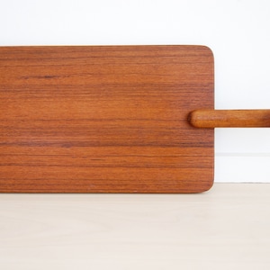 May include: A rectangular wooden serving tray with a long handle. The tray is made of light brown wood with a natural grain pattern.