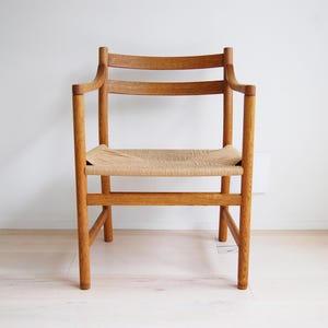 May include: A wooden armchair with a woven seat. The chair has a light brown finish and a curved backrest. The seat is made of woven natural fibers. The chair is a classic design.