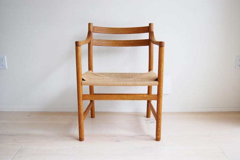 May include: A wooden armchair with a woven seat. The chair has a light brown finish and a curved backrest. The seat is made of woven natural fibers. The chair is a classic design.