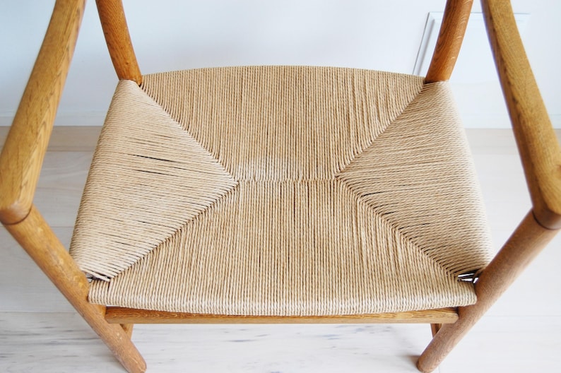 May include: A light-colored wooden chair with a woven seat. The seat is made of tightly woven, light tan rope. The chair's frame is made of light-colored wood. The chair has a classic, minimalist design.