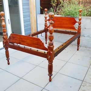 May include: A wooden bed frame with four posts and a headboard. The frame is made of dark wood and has a simple design. The bed is missing a mattress and bedding.