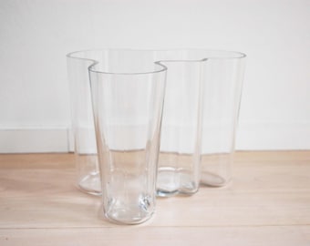 May include: A clear glass vase with a unique, wavy design. The vase has three openings, creating a modern and stylish look.