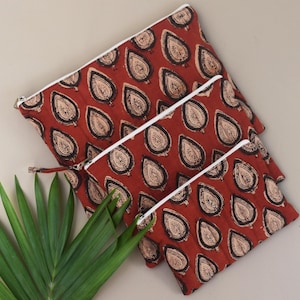 May include: Three red fabric pouches with a leaf pattern in black and beige. Each pouch has a white zipper. The pouches are arranged in a nested fashion, with the largest pouch on top and the smallest on the bottom.