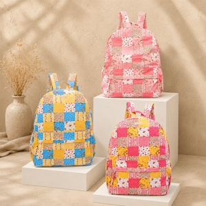 May include: Three backpacks featuring a patchwork design of various floral and gingham patterns. One backpack is primarily pink, one is primarily blue and yellow, and one is a mix of pink, yellow, and red. Each has a top handle and shoulder straps.