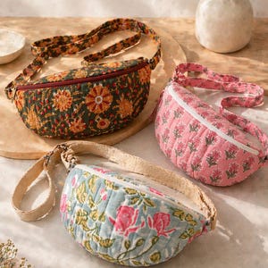 May include: Three quilted fanny packs with floral designs. One is dark green with orange and red flowers, another is pink with a repeating floral print, and the third is light blue with pink roses. Each has a zip closure and an adjustable strap.