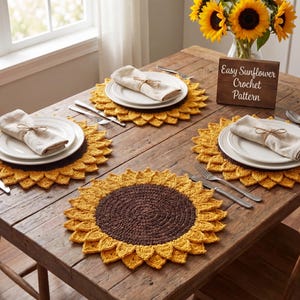 May include: A rustic wooden table set with four sunflower-shaped crochet placemats. Each placemat has a brown center and yellow petals, with white plates and folded napkins. A small wooden sign reads "Easy Sunflower Crochet Pattern".