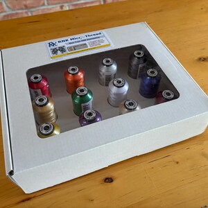 May include: A white cardboard box with a clear rectangular window containing twelve spools of RNK Micro Thread in various colors including red, orange, green, purple, white, silver, gold, and black, with a product label on the top lid.
