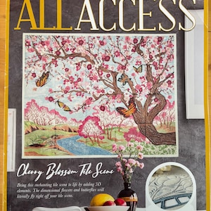 May include: The Anita Goodesign May 2018 All Access magazine cover features a Cherry Blossom Tile Scene embroidery project. The image displays a landscape with a large tree, pink blossoms, butterflies, and a river, alongside a vase of flowers.