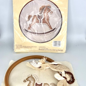 May include: A Stenciled Quick-Wicking rocking horse embroidery kit in a plastic package with a printed image of a brown rocking horse. The kit includes a 6-inch framing hoop, a piece of cotton muslin with a printed design, and bundles of cotton yarn.