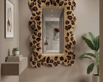 Puede incluir: Un espejo de pared rectangular con un marco grueso, ondulado y copetudo con un patrón de leopardo en color tostado y marrón oscuro. El espejo tiene una superficie de vidrio lisa y reflectante que muestra el reflejo de un pasillo.