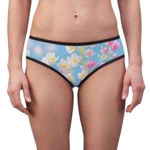 Puede incluir: Ropa interior con fondo azul claro y un patrón floral de flores blancas y rosas. La prenda tiene una cintura negra y un borde festoneado negro a lo largo de las aberturas de las piernas, creando un contraste con el estampado floral.