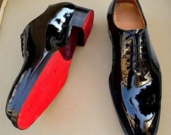 May include: Pair of glossy black leather dress shoes with red soles. The shoes have a classic lace-up design and a polished finish, reflecting light. The red soles add a bold contrast to the black leather.