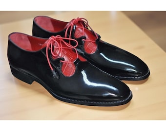 May include: A pair of black patent leather dress shoes with red leather accents and laces. The shoes have a glossy finish and a classic design, suitable for formal occasions.