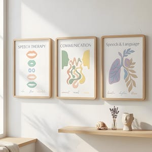 Op de afbeelding: Drie ingelijste kunstprints met houten frames. De prints tonen abstracte illustraties en tekst gerelateerd aan logopedie, communicatie en spraak & taal. Het kleurenpalet omvat zachte pasteltinten. Een plank eronder toont decoratieve items.