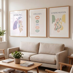 Pode incluir: Três impressões de arte emolduradas com molduras de madeira penduradas acima de um sofá bege. As impressões apresentam designs minimalistas com texto em alemão: "ATMUNG" (respiração), "SPRECHEN" (falar) e "KOMMUNIKATION" (comunicação).