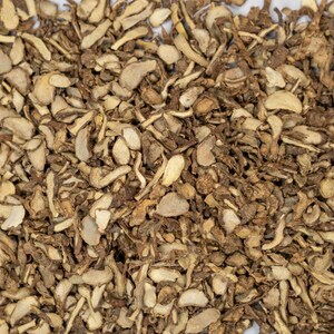 May include: A close-up of dried ginger root pieces. The pieces are chopped and vary in size and shape, with light tan and darker brown colours. The texture appears rough and fibrous, typical of dried ginger.